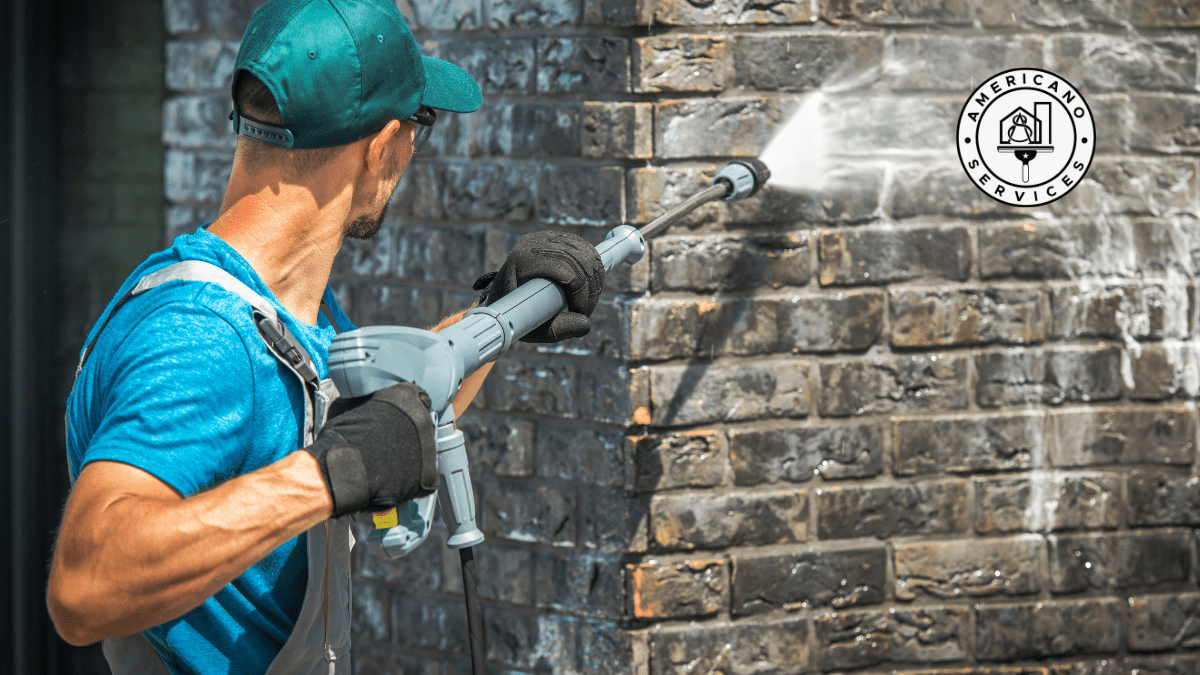 A man with a power washer spraying water on the side of a building.