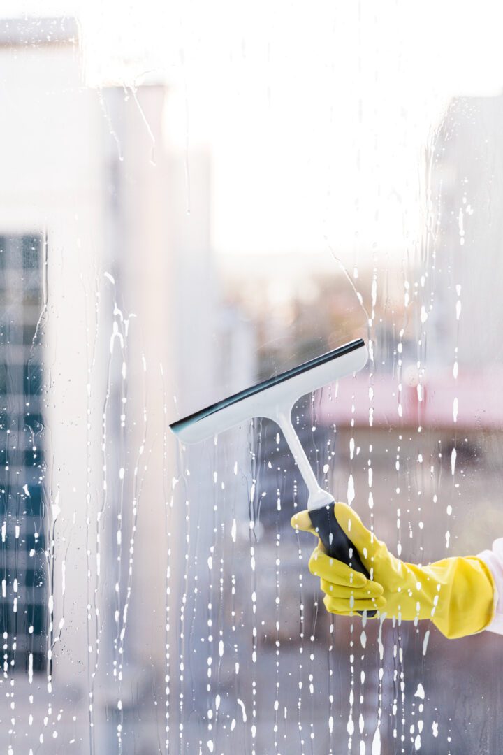 A person in yellow gloves holding a window cleaner.