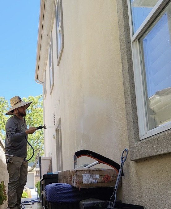 A man in a hat is spraying paint on the outside of a building.