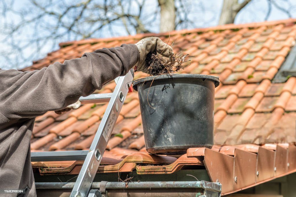 Person cleaning roof gutters with a bucket.