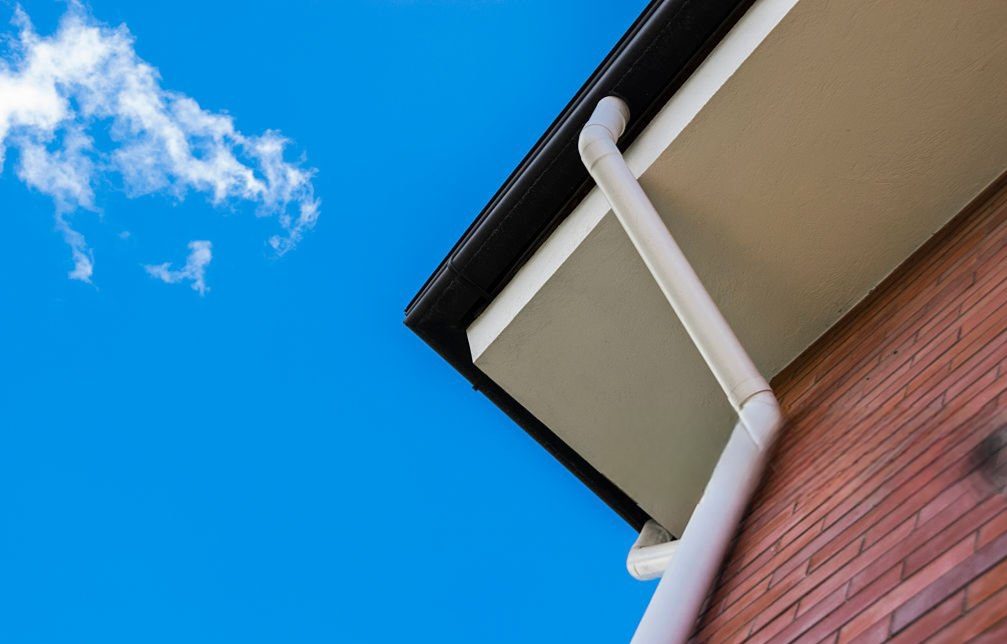 White downspout on brick house against blue sky.