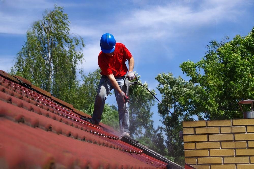 Man cleaning a red roof with a pressure washer.