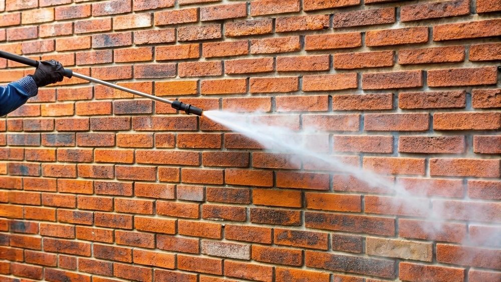 Person cleaning brick wall with pressure washer.