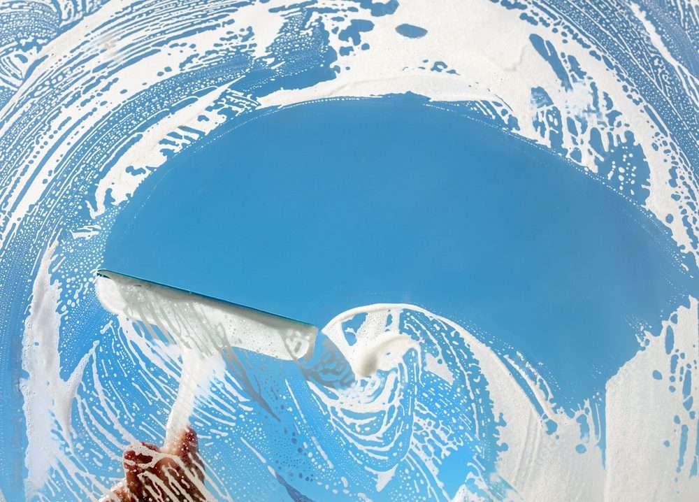 Squeegee cleaning a window with soap suds.