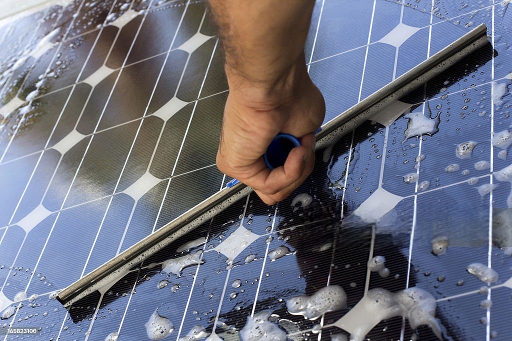 A hand squeegeeing a solar panel.