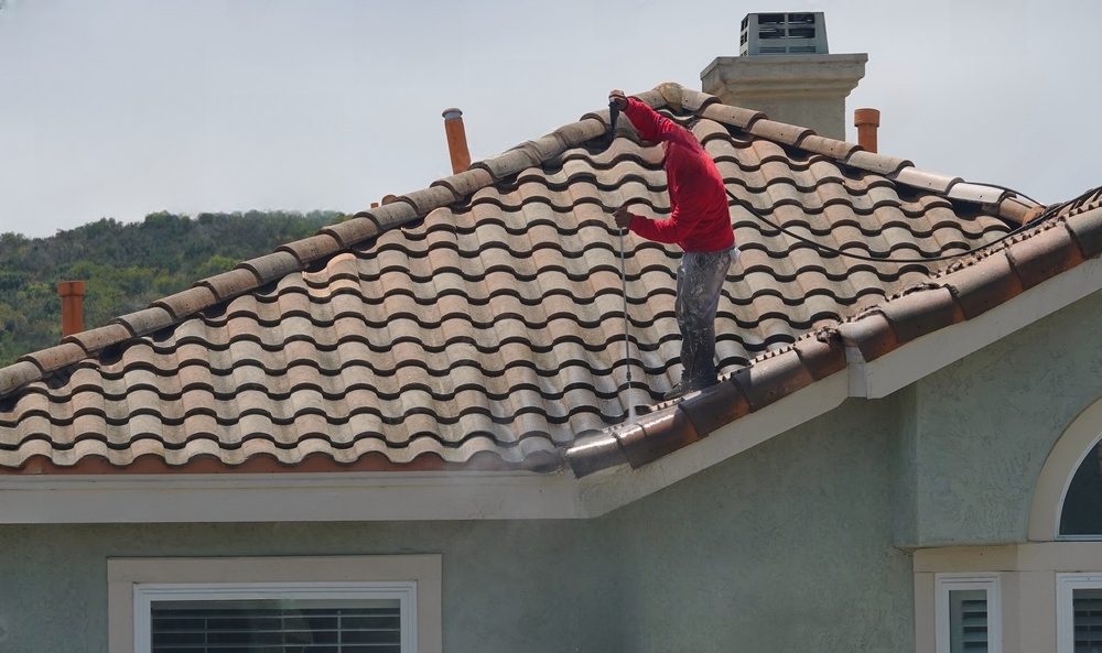 Man pressure washing a tiled roof.