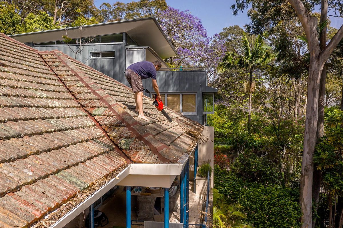 Man blowing leaves off roof with blower.