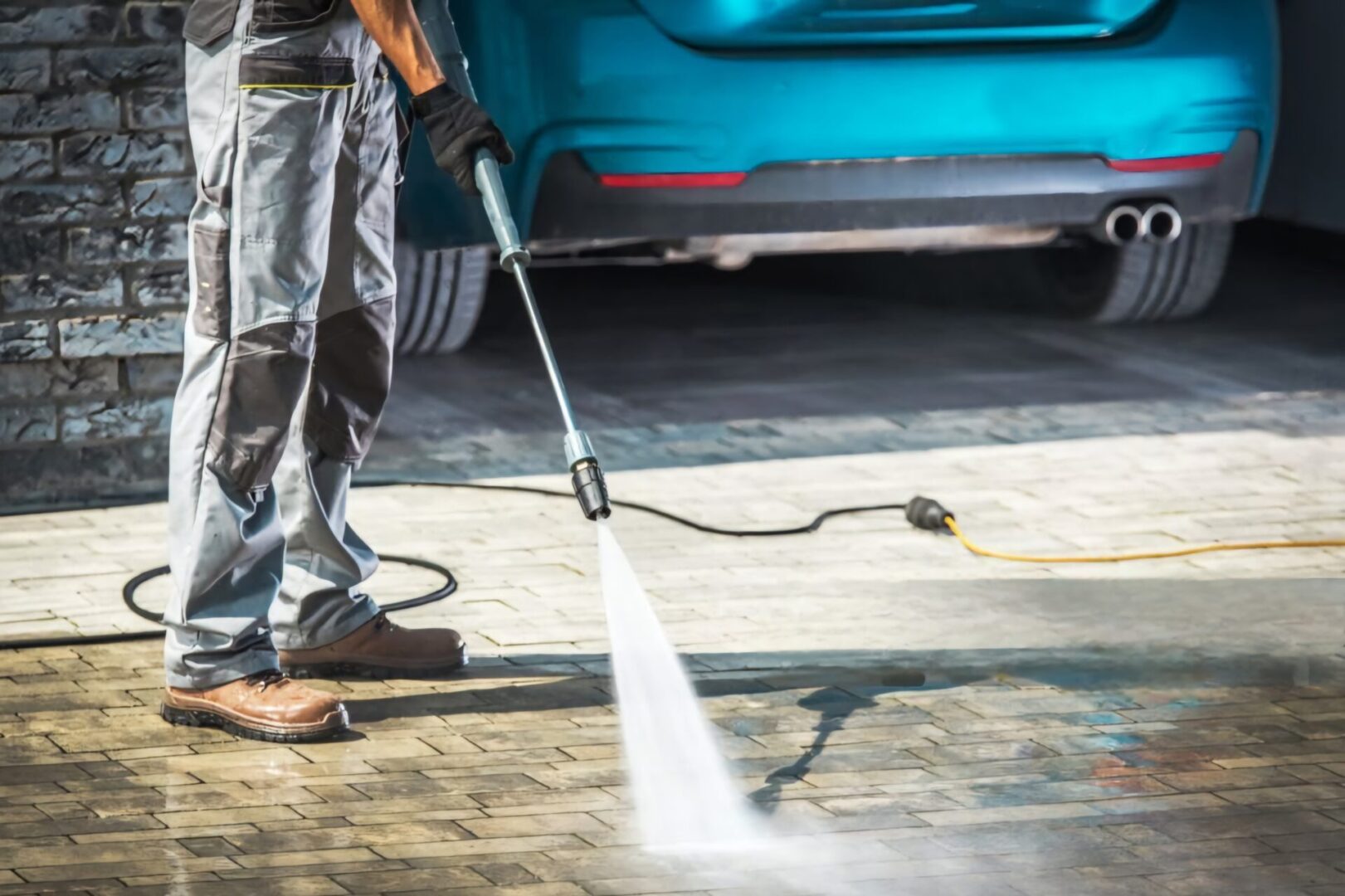 Person pressure washing driveway with blue car.