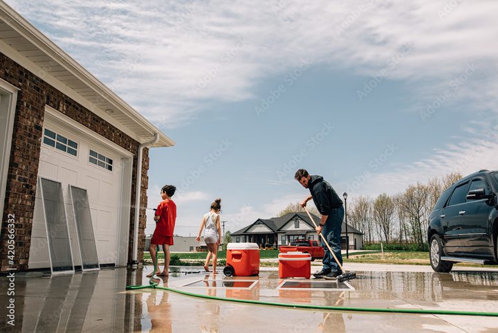 Family cleaning driveway with coolers and car.