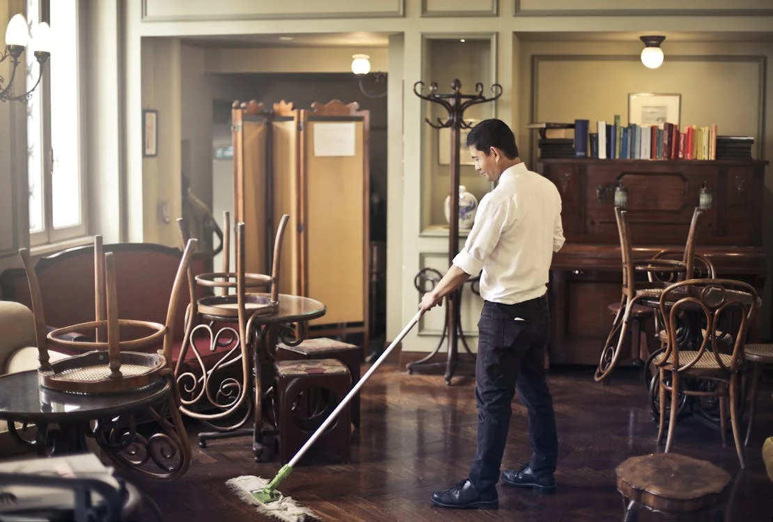 Man mopping wooden floor in cafe.