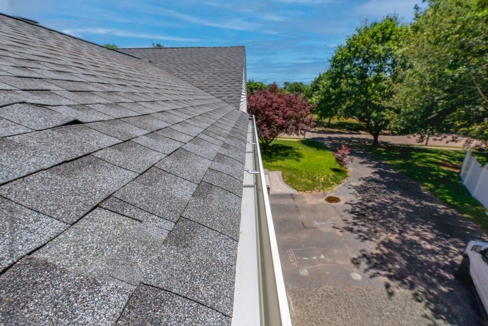 Grey asphalt roof with gutter and yard.