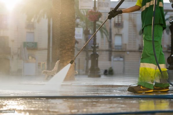 Person power washing sidewalk with a hose.