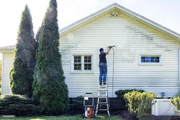 Man pressure washing a white house.