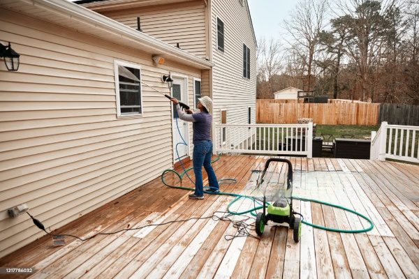 Woman power washing deck with pressure washer.