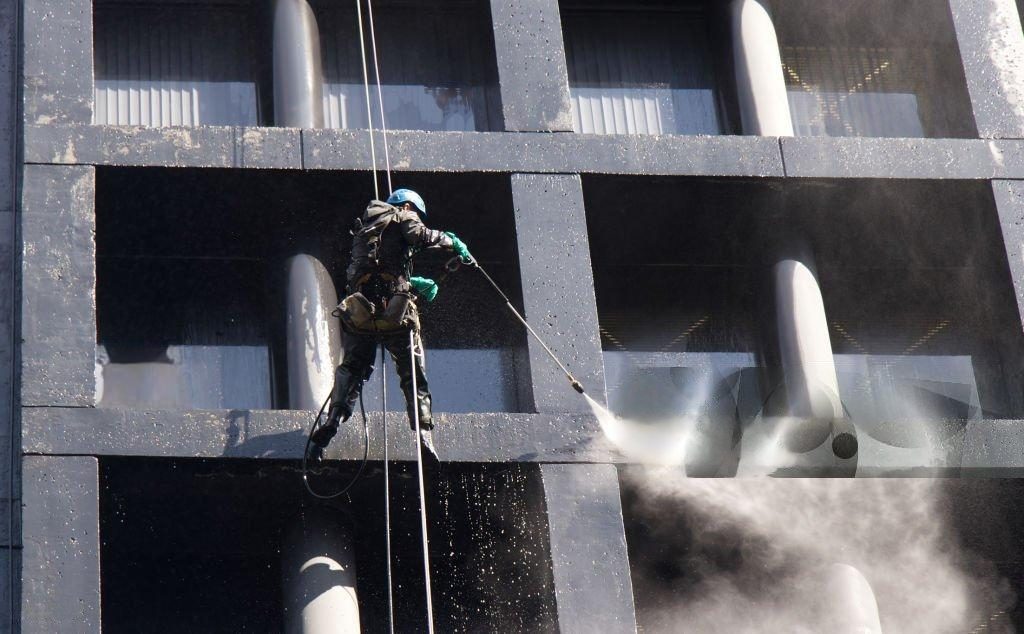 Window cleaner using pressure washer on a building.