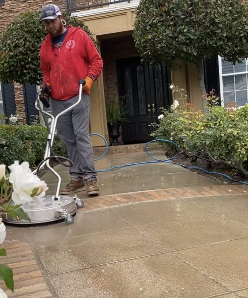 A man is cleaning the sidewalk with a power washer.